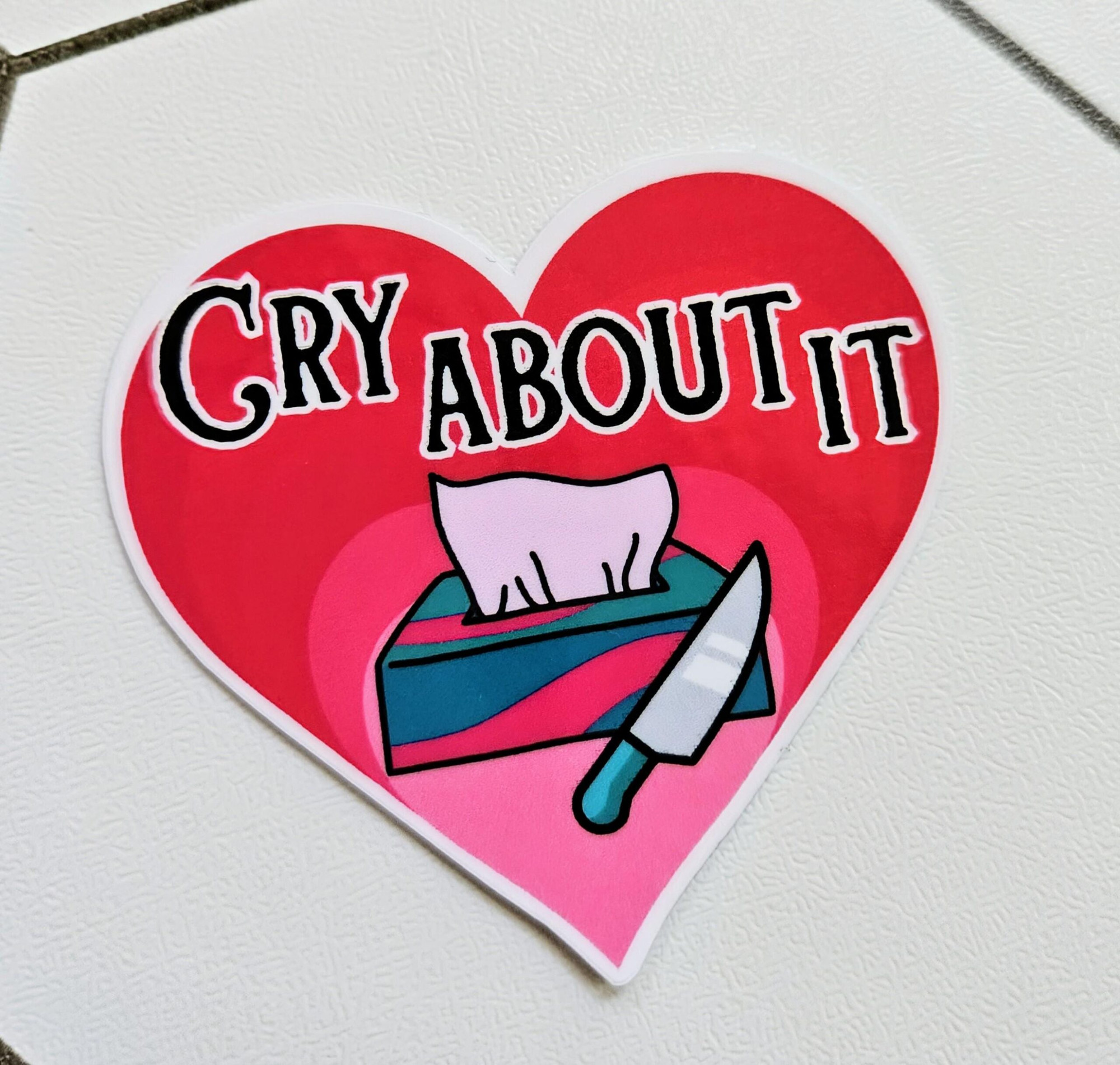 jCry About it Sticker a heart shaped sticker with a picture of a box of tissues and a knife